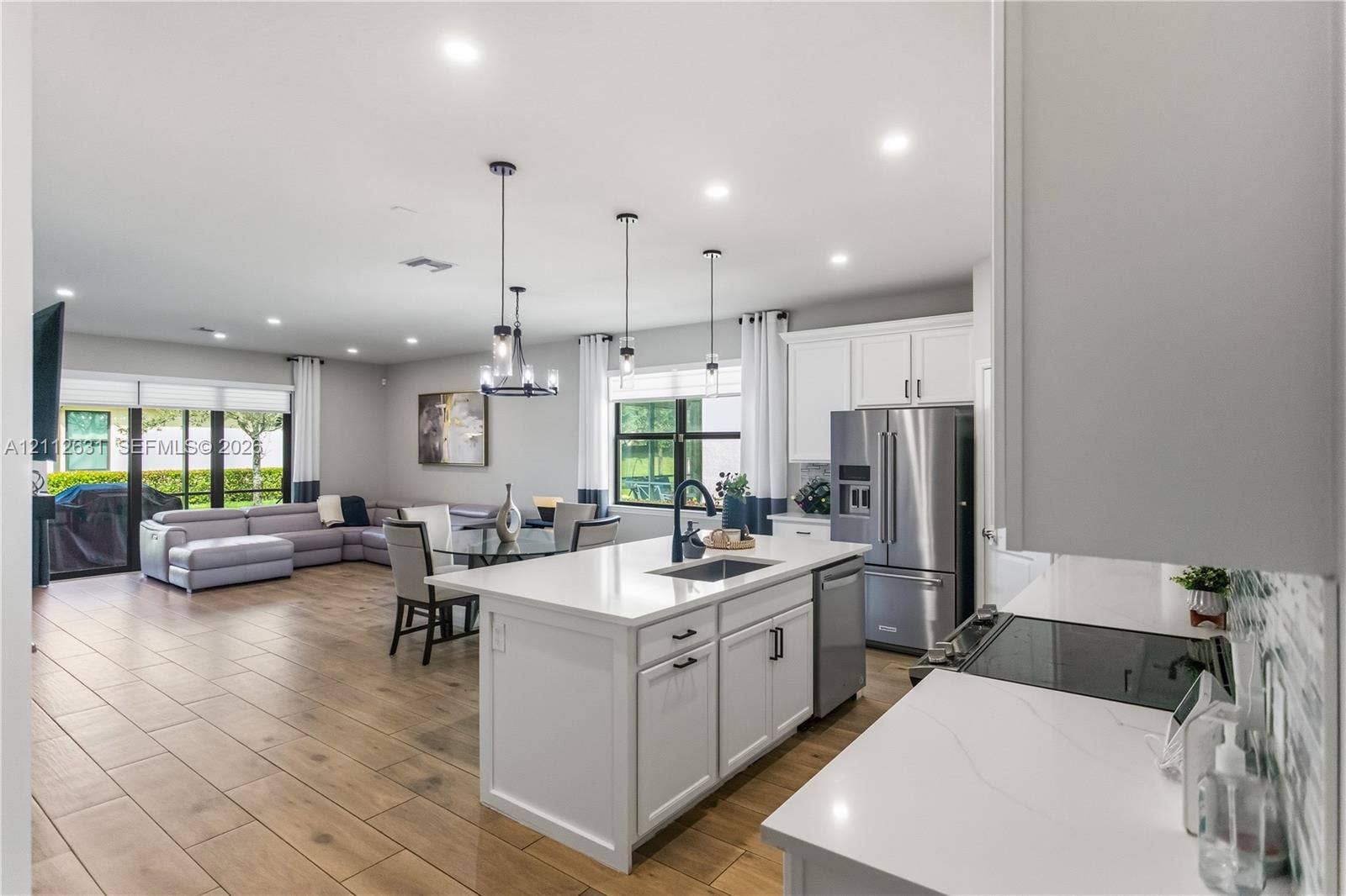 8257 NW 79th Avenue, Tamarac, FL 33321 Kitchen featuring white shaker-style cabinetry, quartz countertops, stainless steel appliances, an island with an undermount sink, and wood-finish tile flooring