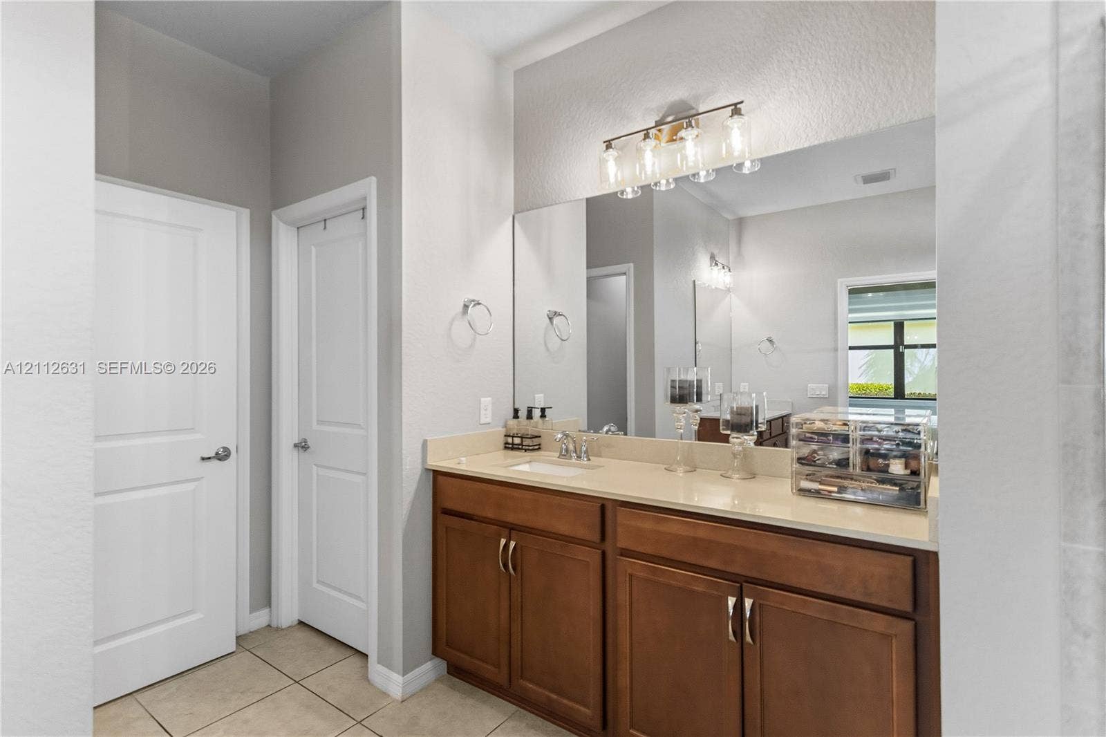 8257 NW 79th Avenue, Tamarac, FL 33321 Bathroom vanity featuring a light-toned countertop, rectangular undermount sink, warm wood-finish cabinetry, a large wall-to-wall mirror, and multi-bulb integrated lighting
