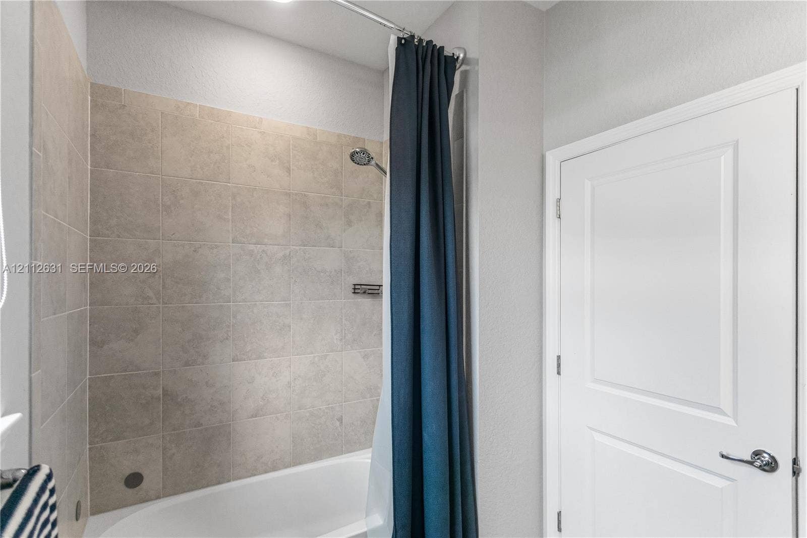 8257 NW 79th Avenue, Tamarac, FL 33321 Bathtub with a shower head, tiled surround, built-in shelving niche, and a panel door with brushed metal hardware