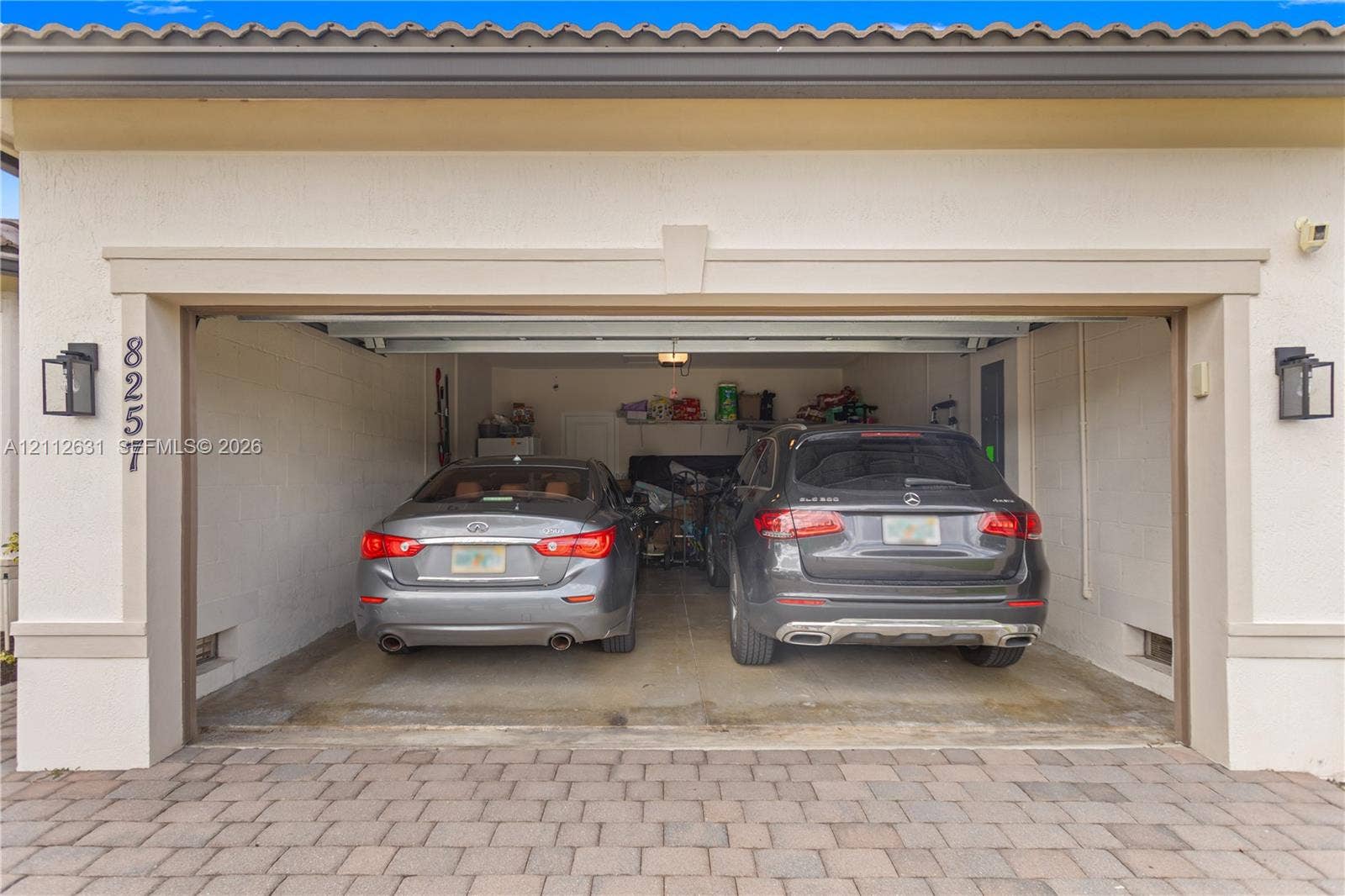 8257 NW 79th Avenue, Tamarac, FL 33321 Two-car garage featuring a concrete floor, stucco exterior finish, tile roof, and wall-mounted exterior lanterns