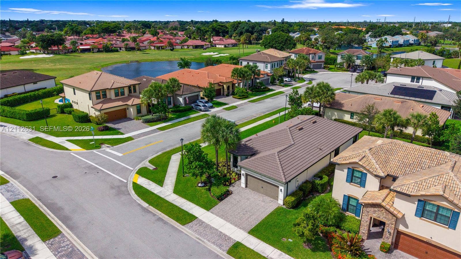 8257 NW 79th Avenue, Tamarac, FL 33321 Aerial perspective of a residential neighborhood featuring paved sidewalks, street lighting, tile roof architecture, paved driveways, and proximity to an expansive grass common area with a water feature