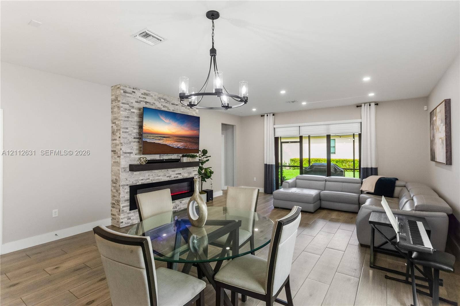 8257 NW 79th Avenue, Tamarac, FL 33321 Open-concept area featuring wood-finish flooring, a floor-to-ceiling stone-cladding fireplace surround, a built-in linear electric fireplace, and a decorative metal chandelier