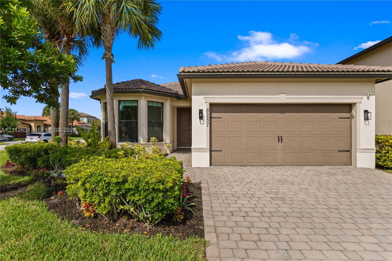 8257 NW 79th Avenue, Tamarac, FL 33321 Stucco exterior featuring a tiled hip roof, multi-pane bay window, paved driveway, and established landscaping