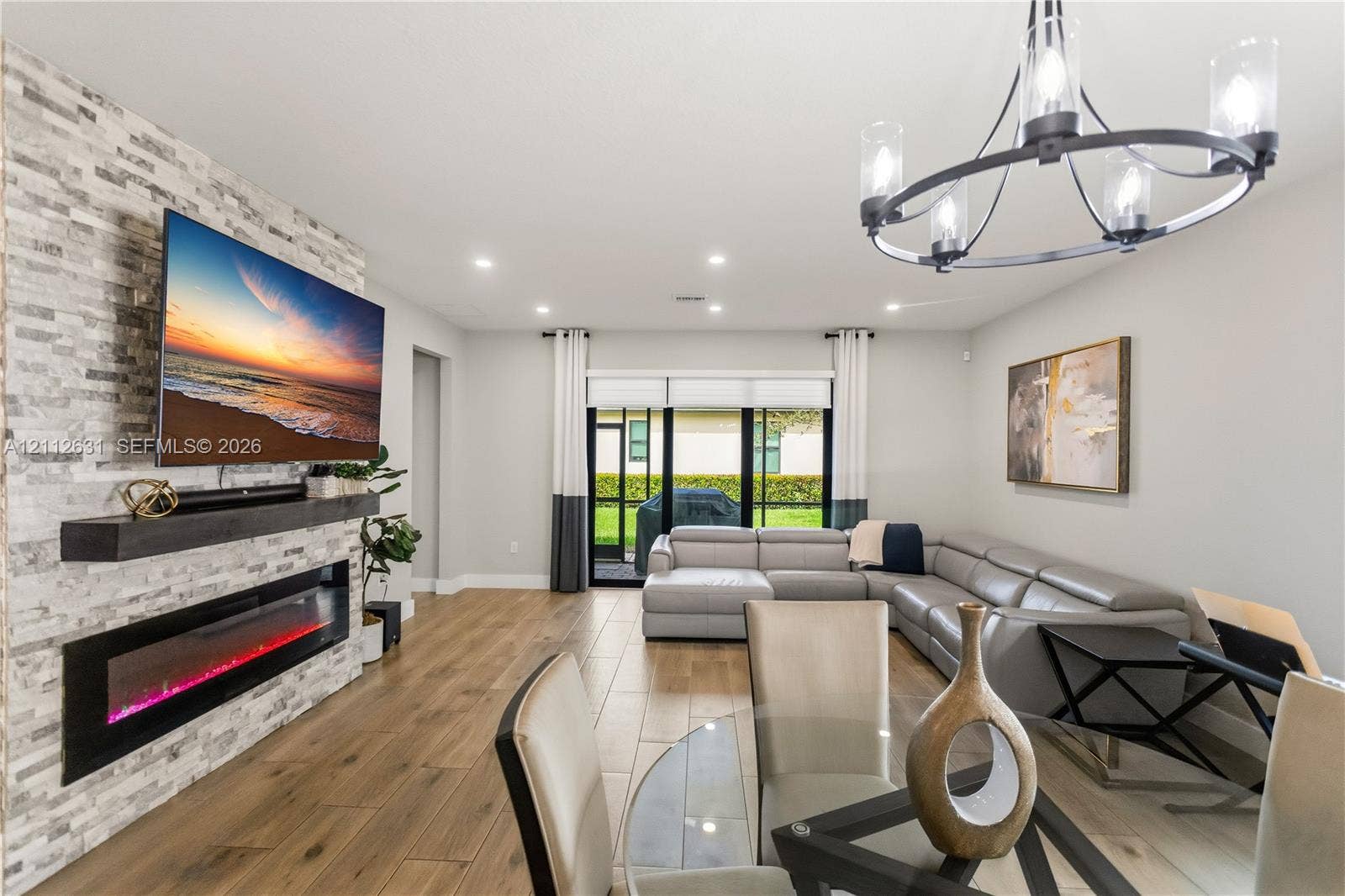 8257 NW 79th Avenue, Tamarac, FL 33321 Stacked stone fireplace feature wall with built-in electric fireplace and dark wood mantel, wood-finish tile flooring, recessed lighting, and chandelier
