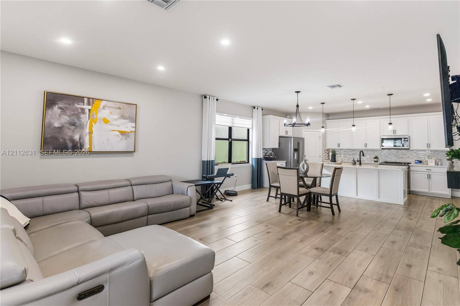 8257 NW 79th Avenue, Tamarac, FL 33321 Open-concept living space featuring wood-finish flooring, recessed lighting, white shaker-style cabinetry, a kitchen island, and a decorative chandelier