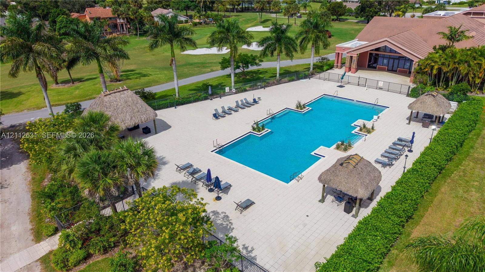 8257 NW 79th Avenue, Tamarac, FL 33321 Rectangular swimming pool featuring a tiled deck, multiple thatched-roof structures, and perimeter landscaping