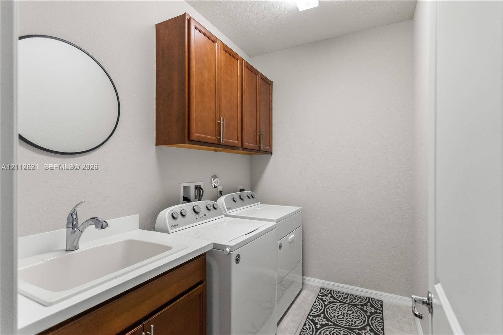 8257 NW 79th Avenue, Tamarac, FL 33321 Laundry room featuring wood-finish cabinetry, a utility sink with a chrome faucet, and solid-surface countertop
