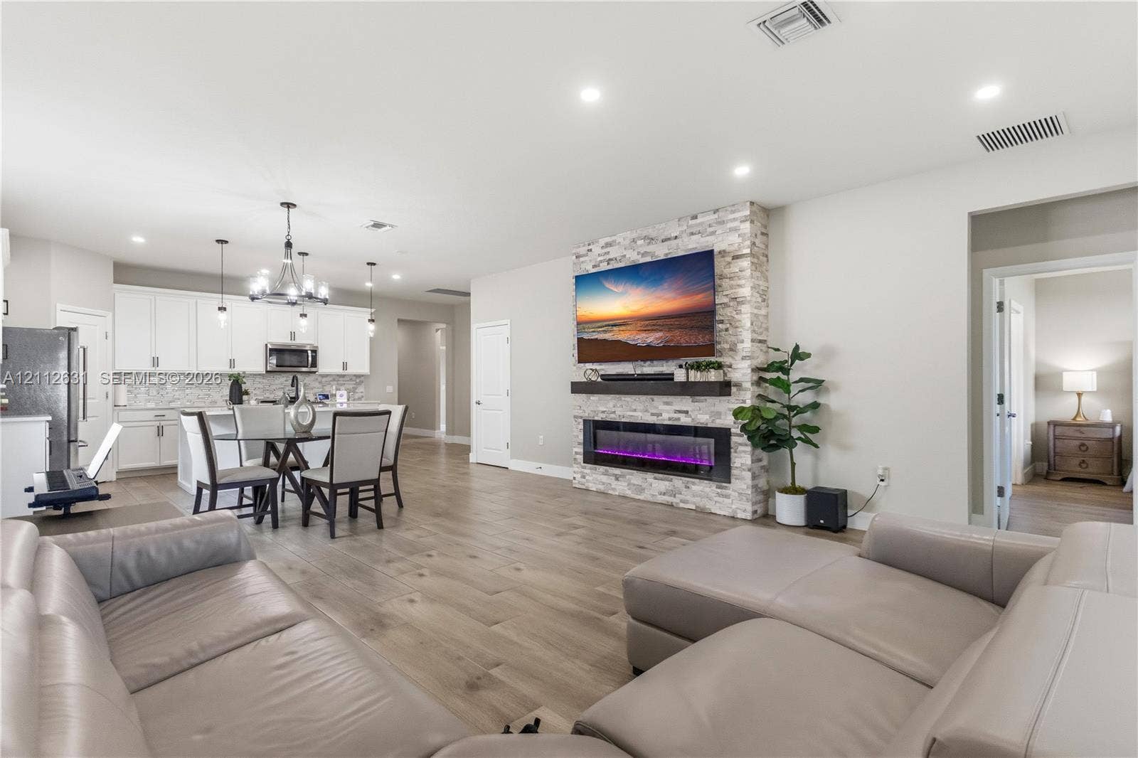 8257 NW 79th Avenue, Tamarac, FL 33321 Open-concept living space featuring wood-finish flooring, recessed lighting, and a floor-to-ceiling stone-veneer fireplace with an integrated electric insert and floating mantel