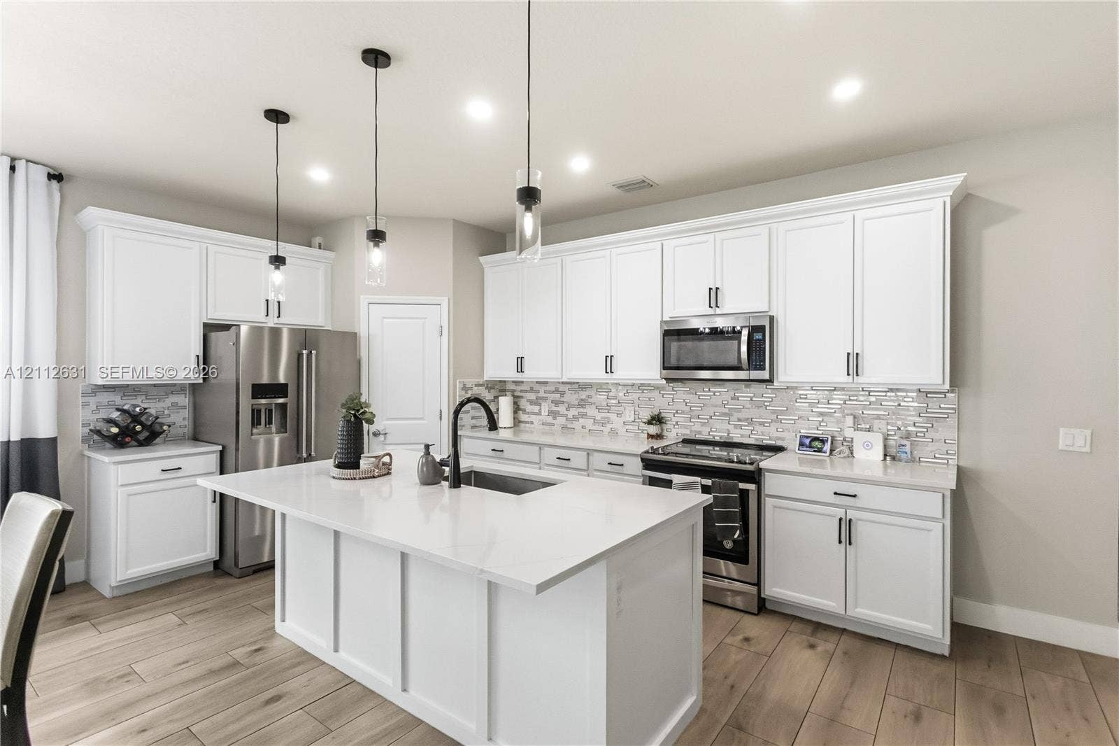 8257 NW 79th Avenue, Tamarac, FL 33321 Kitchen featuring white cabinetry, quartz countertops, a central island with a sink, stainless steel appliances, and wood-finish flooring
