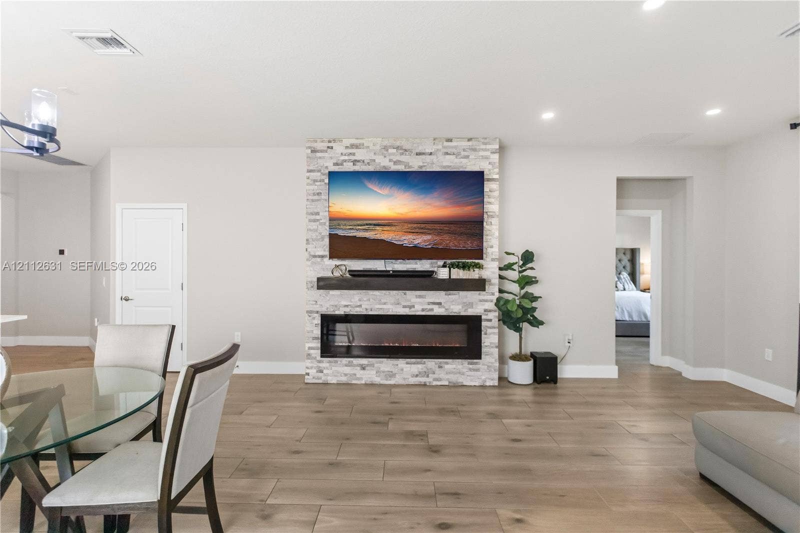 8257 NW 79th Avenue, Tamarac, FL 33321 Floor-to-ceiling stone veneer fireplace surround with a linear electric hearth, wood-finish flooring, and recessed ceiling lighting