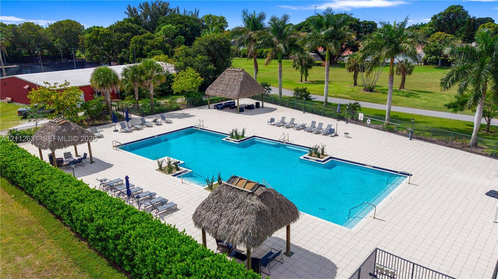 8257 NW 79th Avenue, Tamarac, FL 33321 In-ground swimming pool featuring a large concrete deck, integrated planters, and multiple thatched-roof cabanas