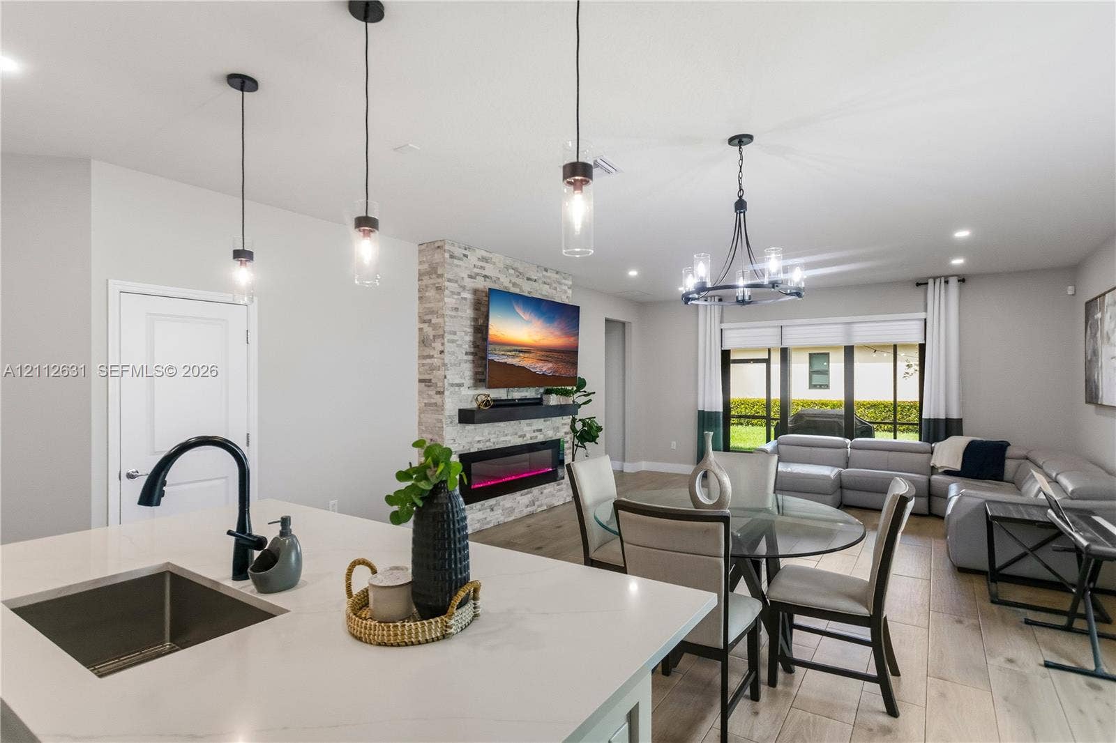 8257 NW 79th Avenue, Tamarac, FL 33321 Open-concept space featuring wood-finish flooring, a kitchen island with a quartz countertop, a matte black faucet, and a floor-to-ceiling stone-clad fireplace with an integrated electric firebox