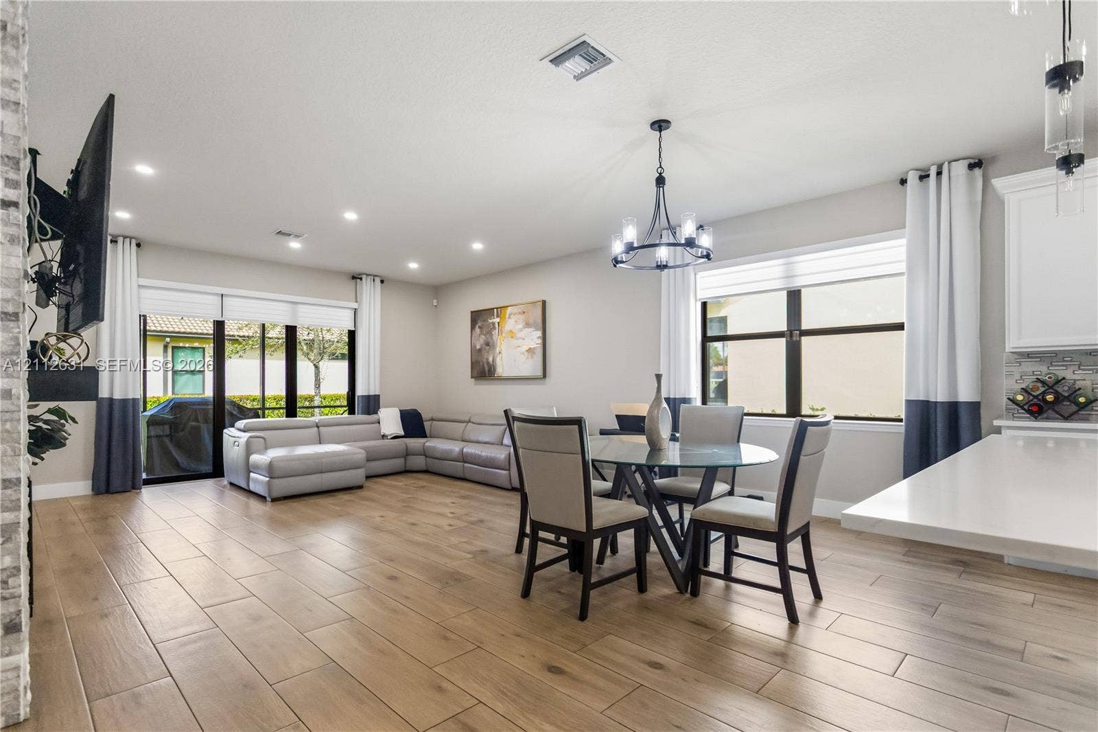 8257 NW 79th Avenue, Tamarac, FL 33321 Open-concept living space featuring wood-finish flooring, recessed lighting, a multi-arm chandelier, large windows with horizontal blinds, and glass sliding doors