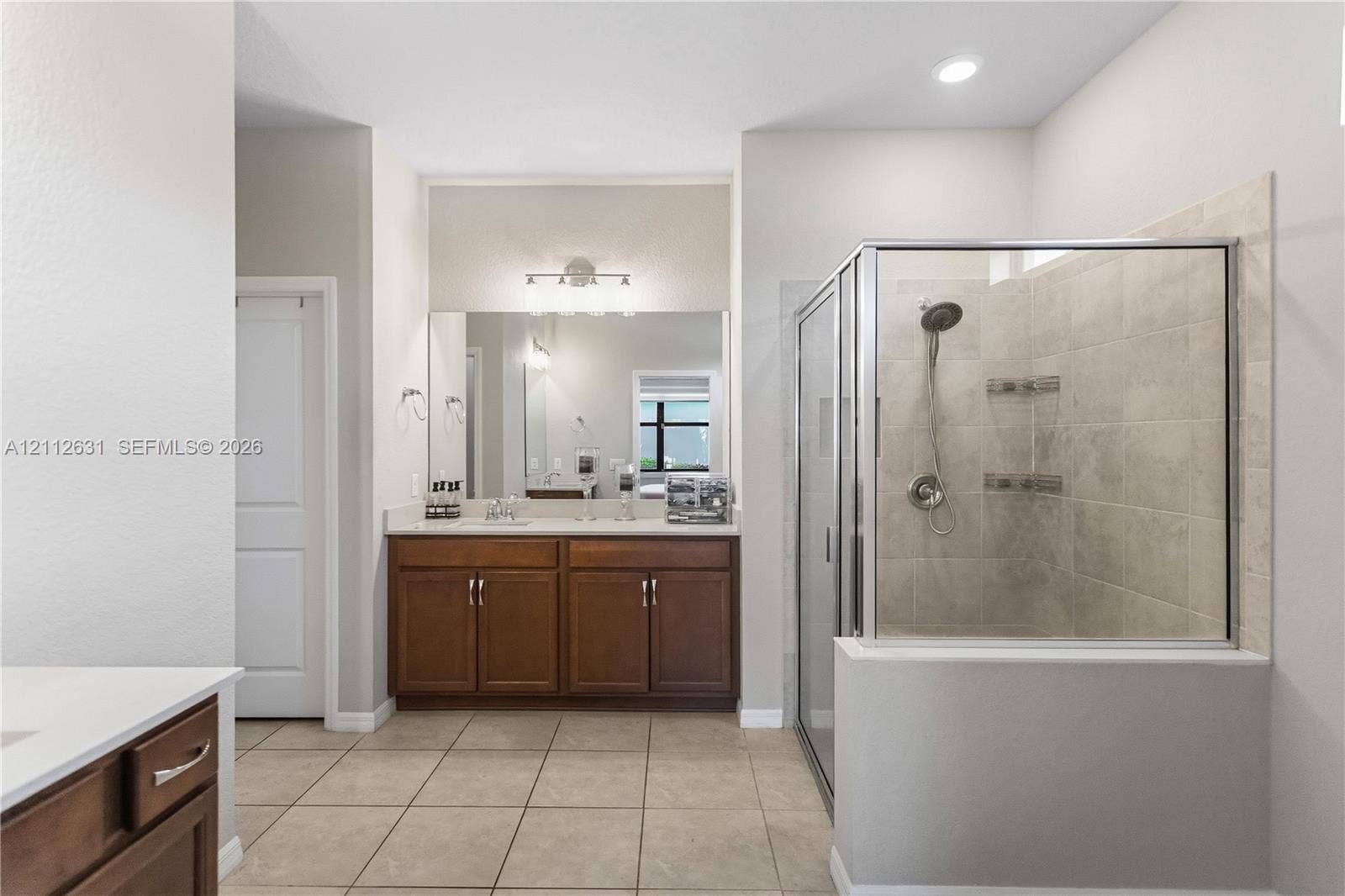 8257 NW 79th Avenue, Tamarac, FL 33321 Dual-sink vanity with stone countertop, large wall-mounted mirror, glass-enclosed shower with tile surround, and tile flooring