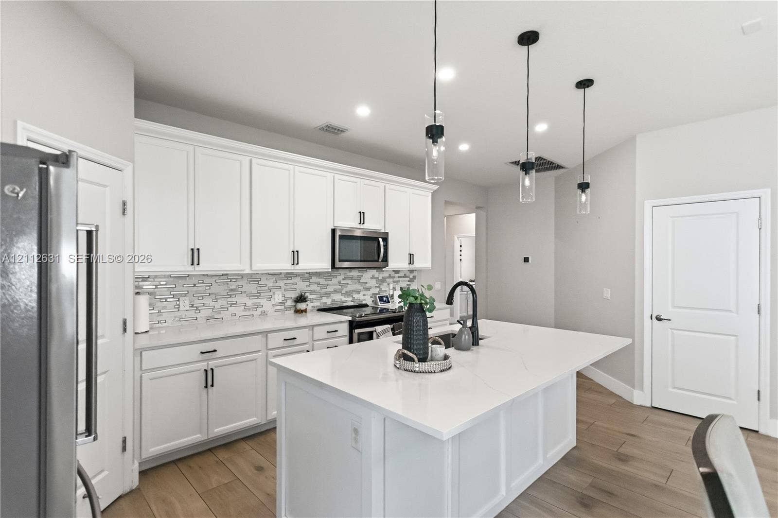 8257 NW 79th Avenue, Tamarac, FL 33321 Kitchen featuring white shaker-style cabinetry, a large central island with a solid-surface countertop, linear tile backsplash, and three glass pendant lights