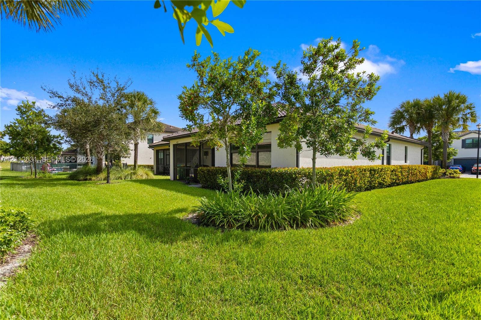 8257 NW 79th Avenue, Tamarac, FL 33321 Stucco exterior featuring a screened-in lanai, mature landscaping, manicured lawn, and multi-pitched roofline