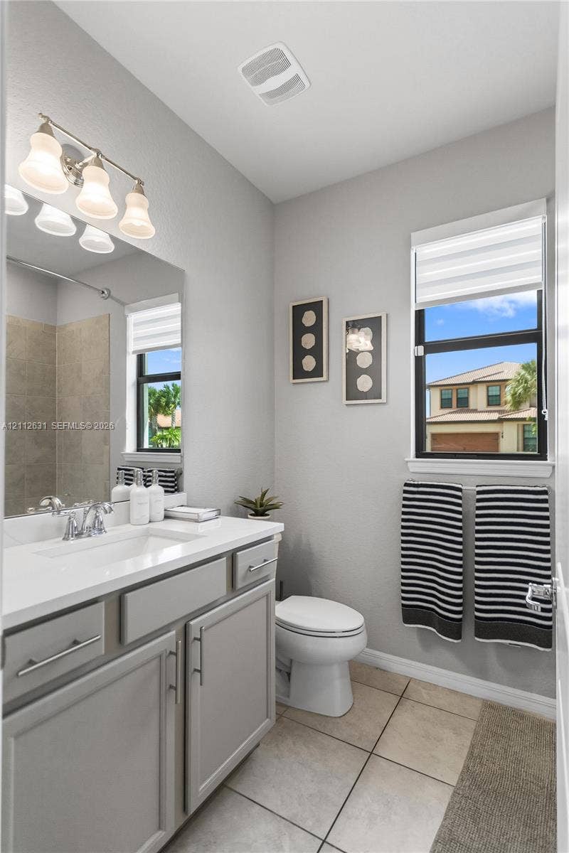 8257 NW 79th Avenue, Tamarac, FL 33321 Bathroom featuring a white countertop vanity with gray cabinetry, a wall-to-wall mirror, a three-light fixture, and ceramic tile flooring