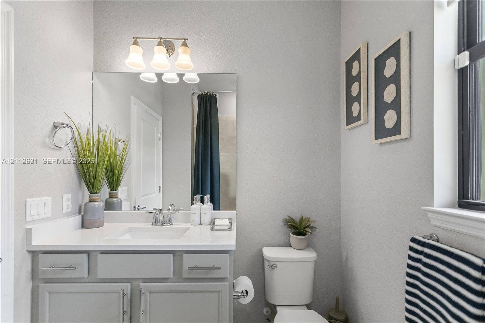 8257 NW 79th Avenue, Tamarac, FL 33321 Bathroom featuring a light-toned vanity with a rectangular undermount sink, solid surface countertop, polished chrome fixtures, and a triple-light wall-mounted fixture above a rectangular mirror