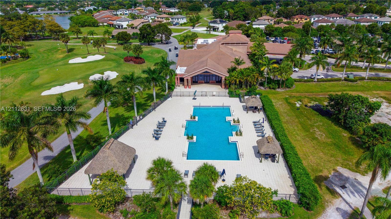 8257 NW 79th Avenue, Tamarac, FL 33321 Community pool with paver decking and multiple thatched-roof structures, positioned alongside a golf course featuring manicured greens and sand bunkers