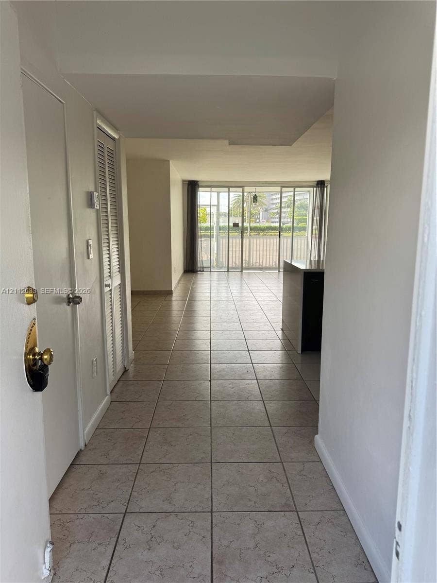 1770 NE 191st Street, #104-1, Miami, FL 33179 Ceramic tile flooring, louvered bi-fold closet doors, and floor-to-ceiling glass sliding doors opening to a balcony