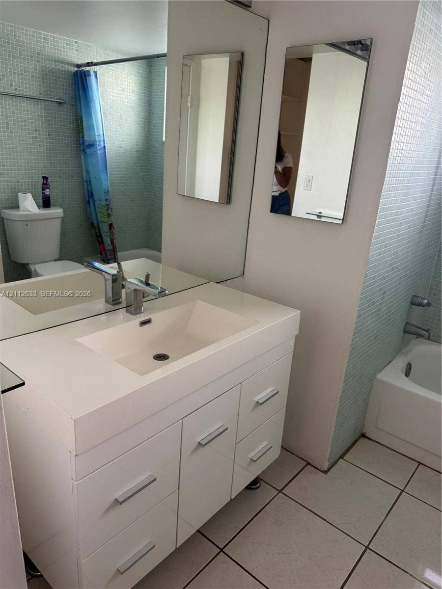 1770 NE 191st Street, #104-1, Miami, FL 33179 Bathroom featuring a white vanity with an integrated sink, brushed metal hardware, a large wall-mounted mirror, light-toned mosaic wall tile, and white floor tile