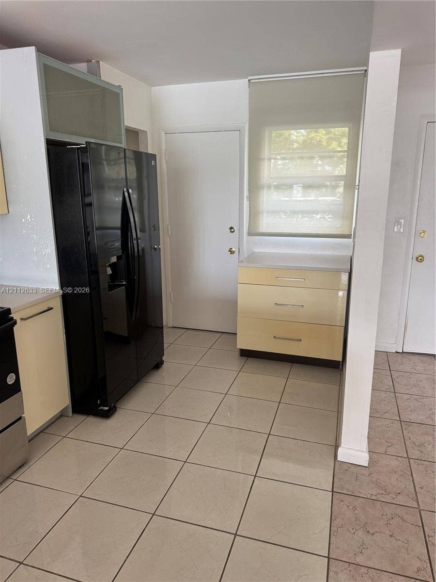 1770 NE 191st Street, #104-1, Miami, FL 33179 Kitchen featuring ceramic tile flooring, glossy flat-panel cabinetry, a built-in black refrigerator, and a solid-surface countertop