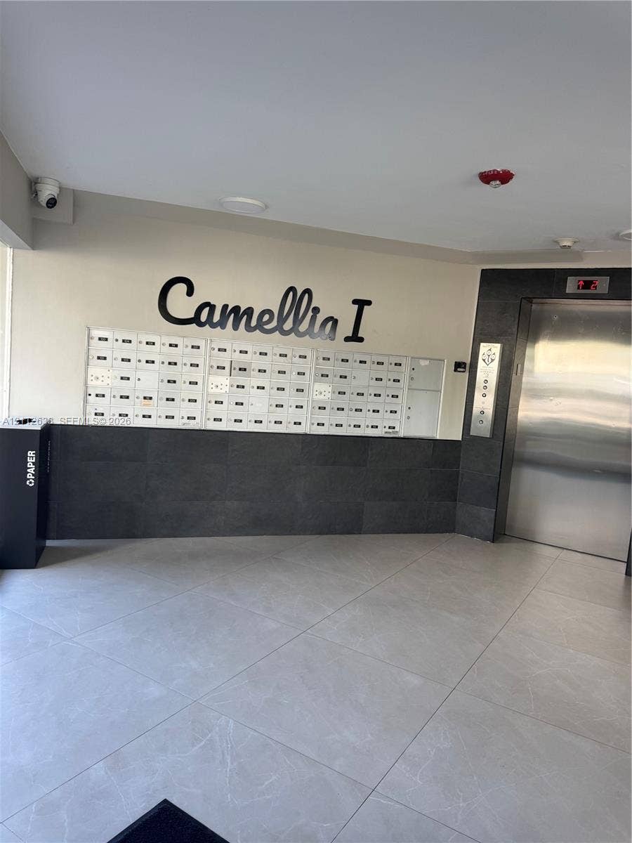 1770 NE 191st Street, #104-1, Miami, FL 33179 Lobby featuring large-format ceramic floor tiling, stainless steel elevator, integrated mailbox bank, and decorative stone wall cladding