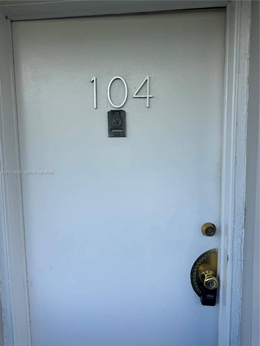 1770 NE 191st Street, #104-1, Miami, FL 33179 Solid door entry featuring metallic house numbering, a peephole, and a brass-tone lever handle set