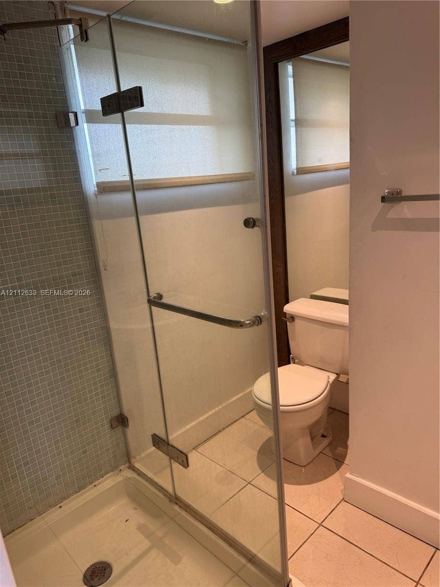 1770 NE 191st Street, #104-1, Miami, FL 33179 Glass-enclosed shower with mosaic tile surround, ceramic floor tiling, and a standard-height porcelain toilet