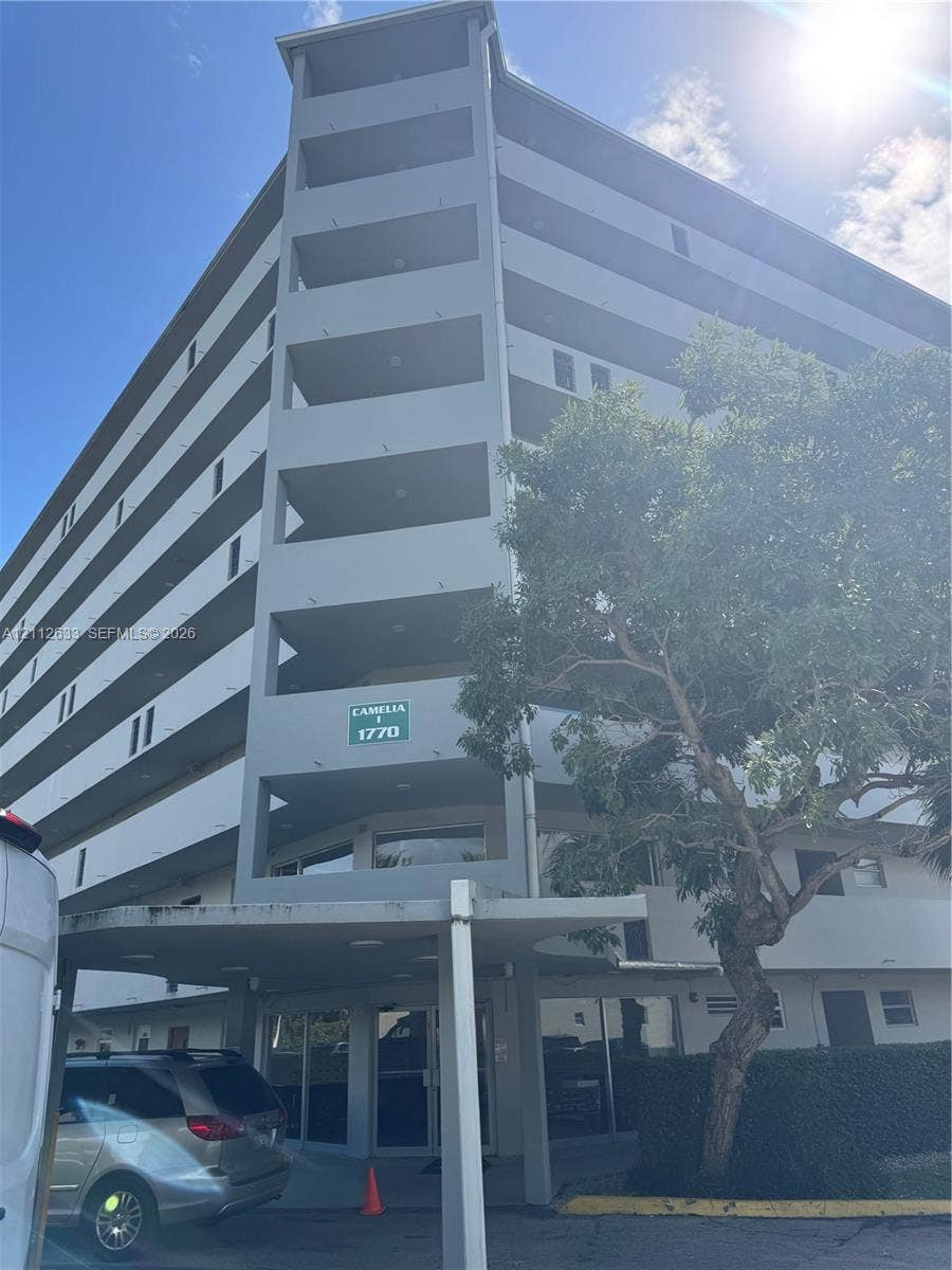1770 NE 191st Street, #104-1, Miami, FL 33179 Multi-story residential building featuring covered exterior balconies, a ground-level covered entryway, and mature landscaping