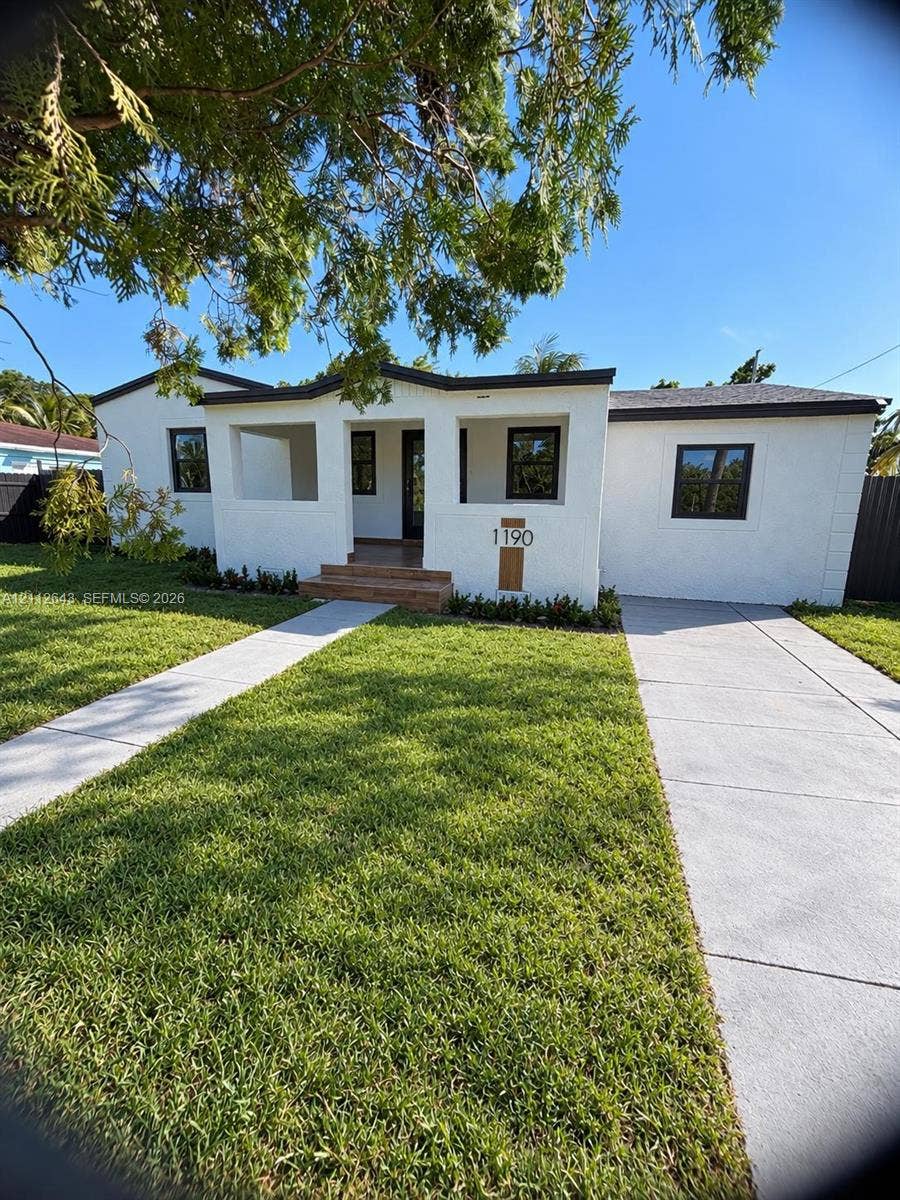 1190 NW 57th Street, Miami, FL 33127 Single-story exterior featuring white stucco finish, a recessed covered entryway, tile-accented steps, and a paved concrete driveway