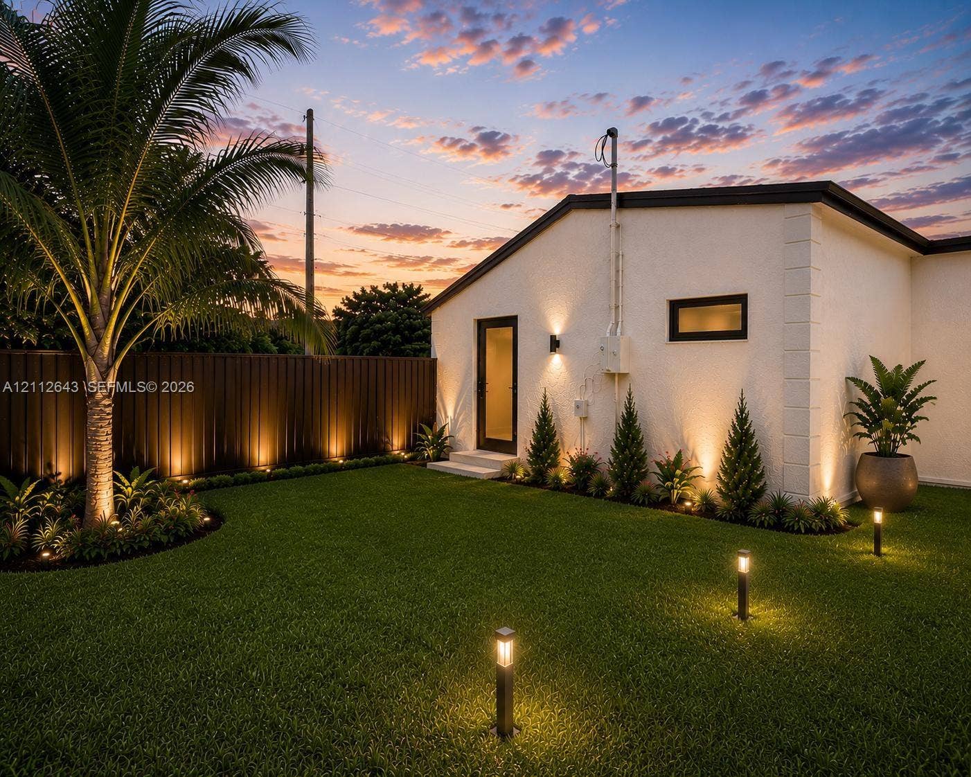 1190 NW 57th Street, Miami, FL 33127 Landscaped backyard featuring a manicured lawn, established palm tree, structural exterior lighting, and private metal fencing