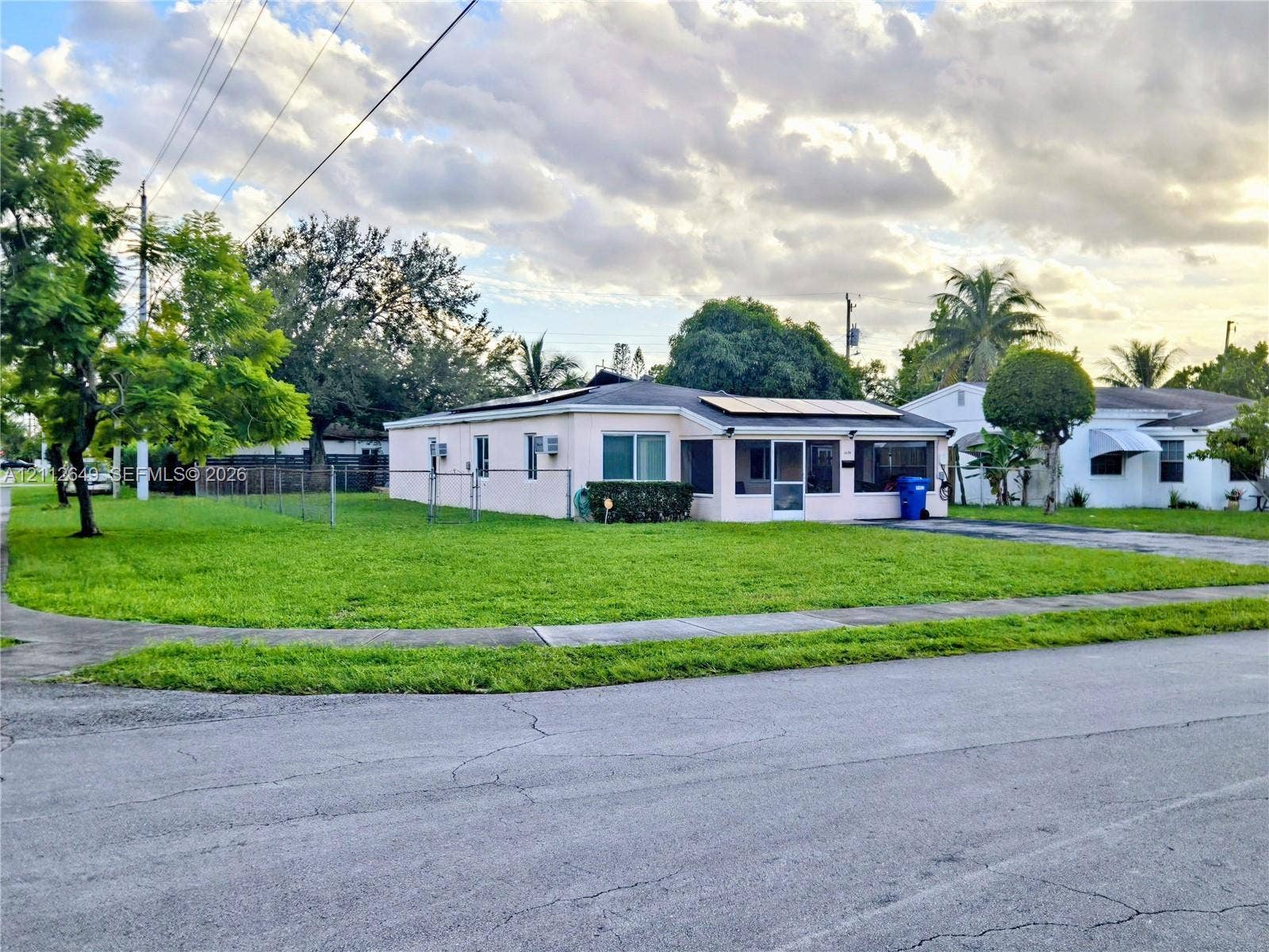 Single-story residence featuring a smooth stucco exterior, integrated rooftop solar panels, a screened-in porch, and a chain-link fenced yard
