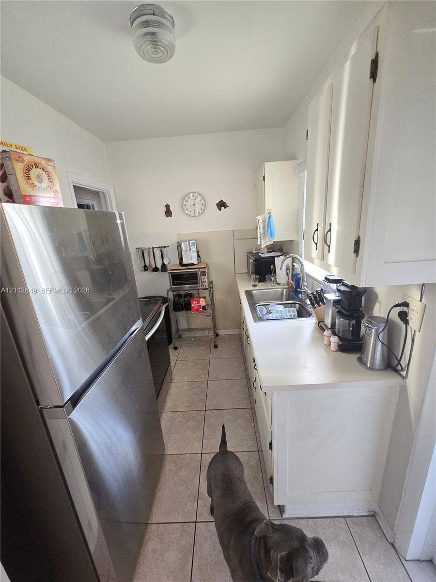 Kitchen featuring white cabinetry, stainless steel refrigerator, stainless steel sink with a high-arch faucet, and tile flooring