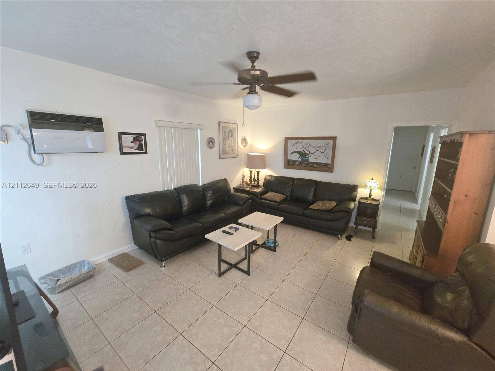 Room interior featuring tile flooring, ceiling fan, wall-mounted climate control unit, and vertical window blinds