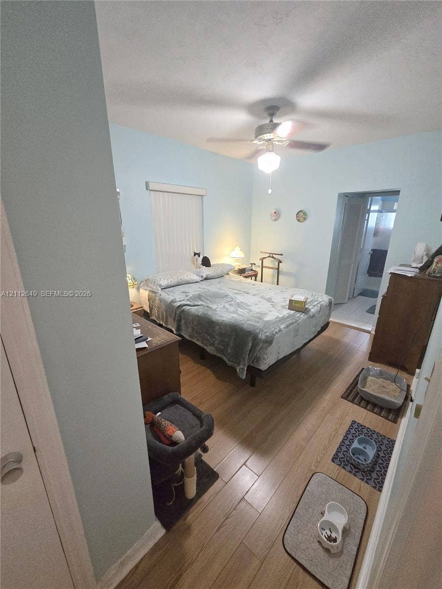 Bedroom featuring wood-finish flooring, vertical blinds, and a ceiling fan with light fixture