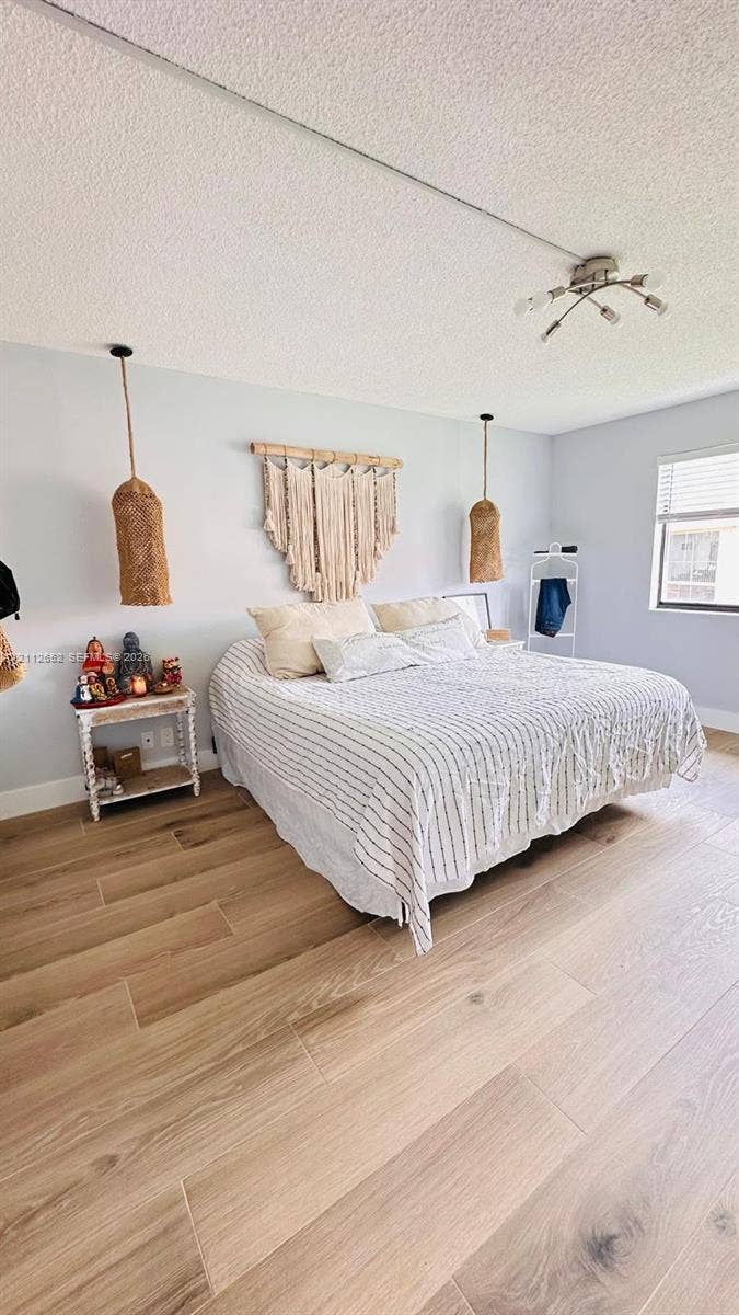 Room featuring light-toned wood-finish flooring, textured ceiling, dual suspended woven light fixtures, and a multi-bulb ceiling-mounted light