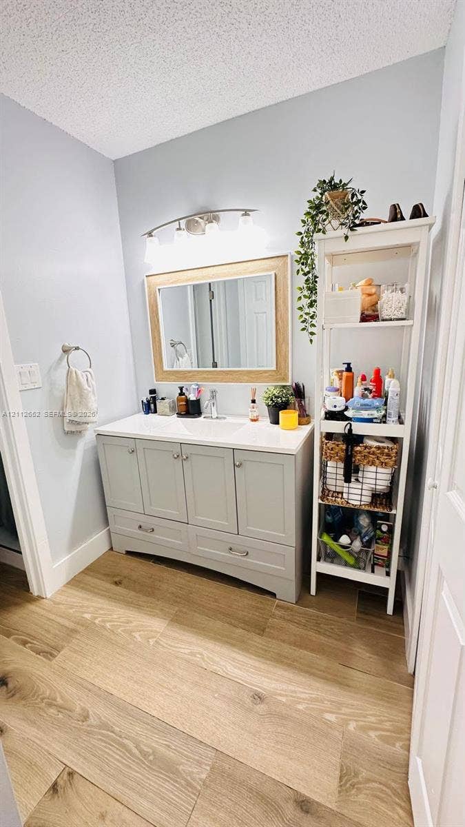 Bathroom vanity with a stone countertop, integrated undermount sink, multi-drawer cabinetry, wood-finish flooring, and a framed mirror