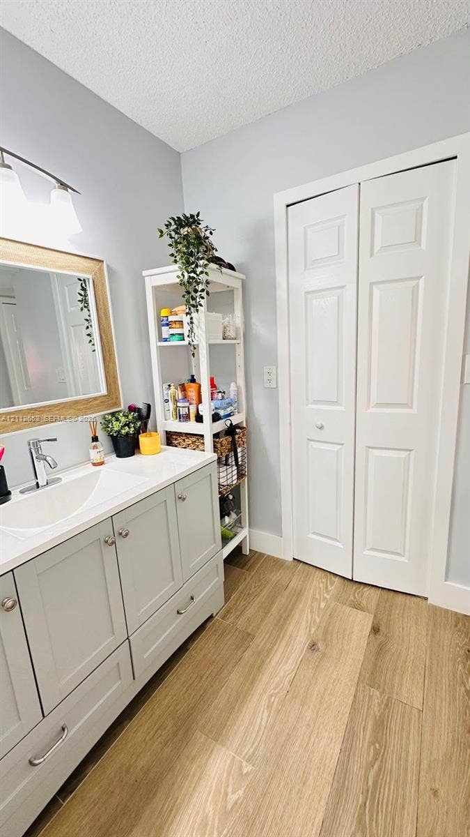 Bathroom vanity with shaker-style cabinetry, integrated rectangular sink, light wood-finish flooring, brushed metal hardware, and bi-fold closet doors