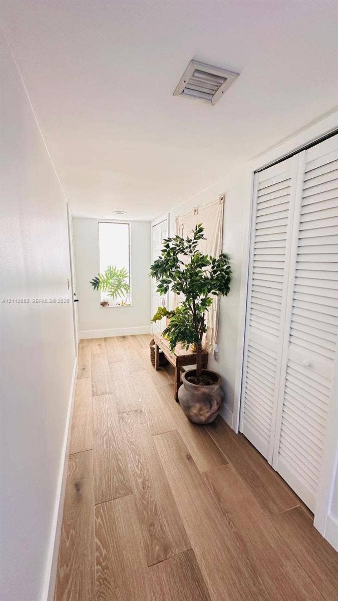 Hallway featuring wood-finish flooring, white louvered closet doors, and an elongated rectangular window