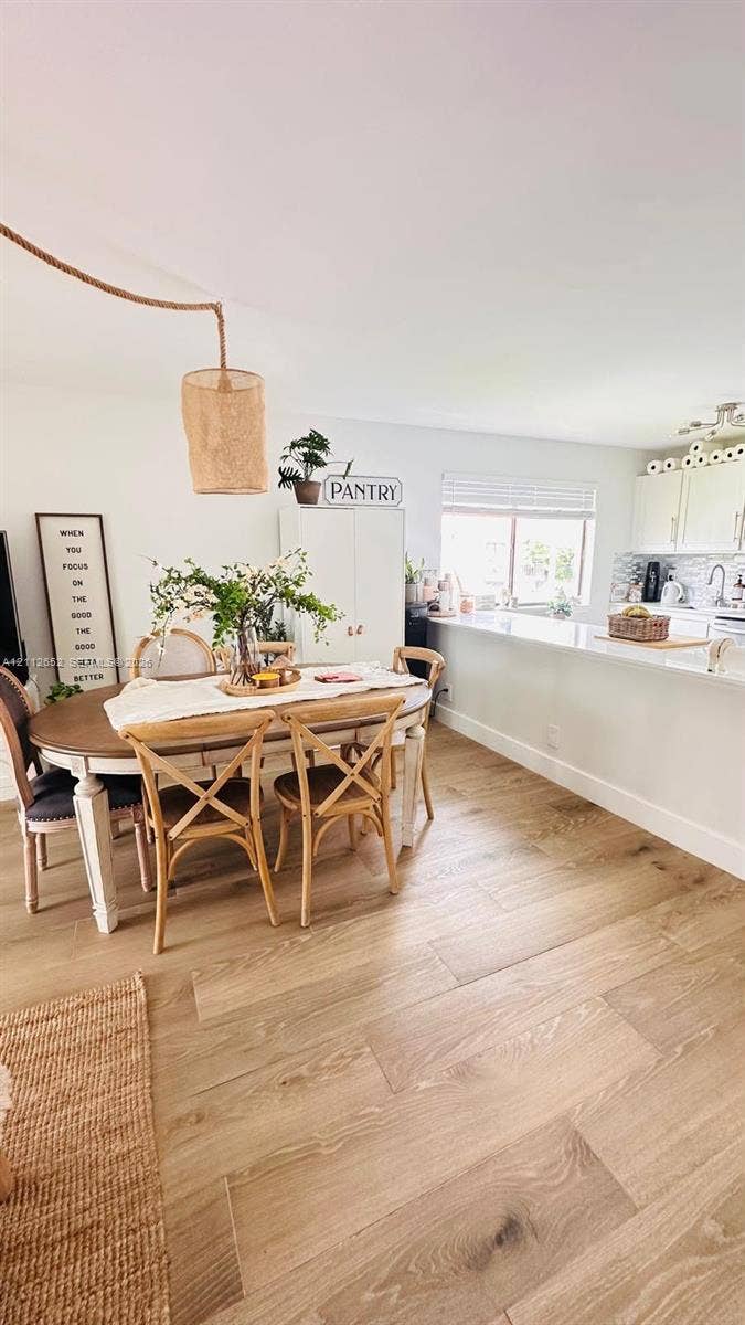 Dining area featuring wood-finish flooring, a suspended woven pendant light, and a peninsula with a stone countertop