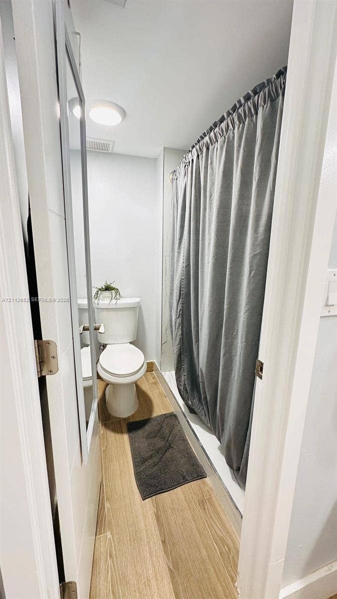 Bathroom featuring wood-finish flooring, a white porcelain toilet, and a tub-shower combination with a ceiling-mounted light fixture