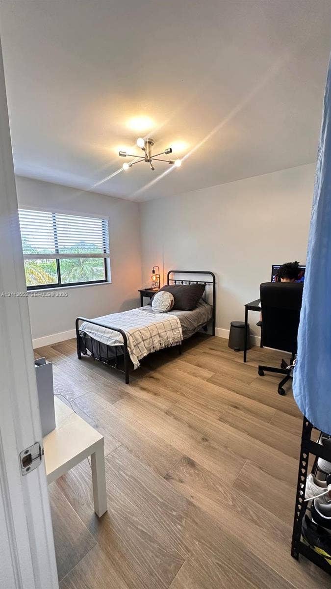 Neutral interior featuring wide-plank wood-finish flooring, a contemporary six-arm chandelier, and a horizontal sliding window with integrated blinds