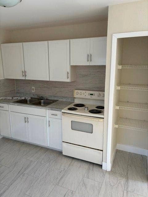 Kitchen featuring white cabinetry with metallic pulls, stone-patterned laminate countertops, integrated double-basin sink, electric range, and a built-in pantry with wire shelving