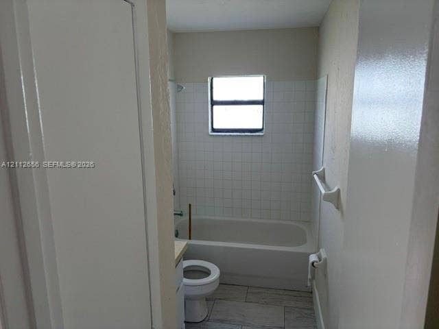 Bathroom featuring a tub-shower combination with white tile surround, a single-basin vanity, and neutral stone-finish tile flooring