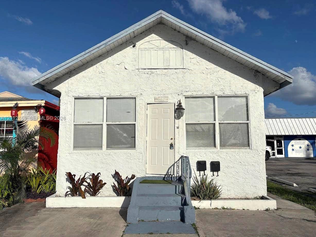 Textured stucco exterior featuring a gable roof, decorative pediment detail, exterior wall-mounted lantern lighting, and a concrete staircase with metal handrail