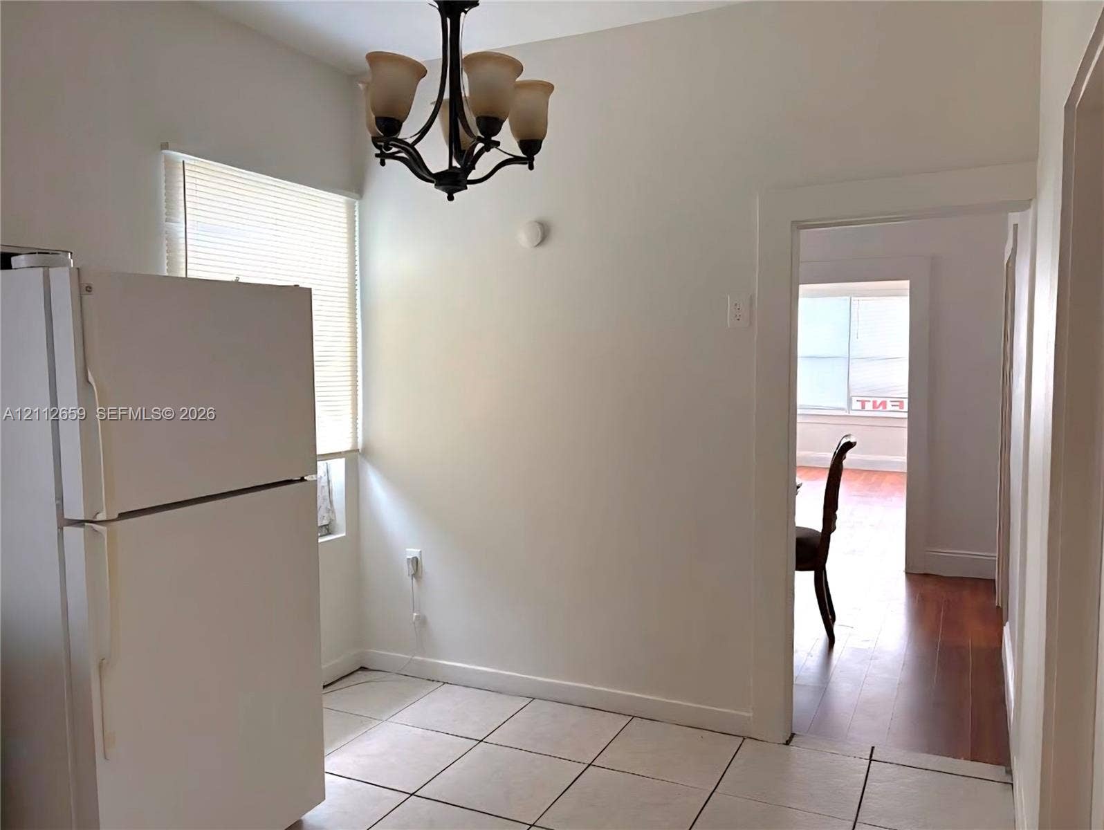 Kitchen area featuring white ceramic floor tiling, a white top-freezer refrigerator, and a dark metal four-arm chandelier with frosted glass shades