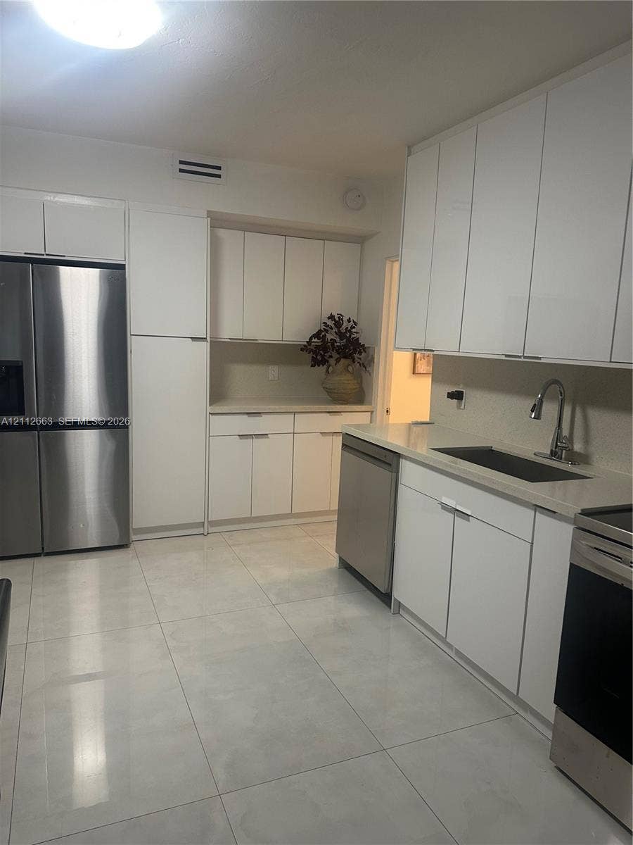 10185 Collins Avenue, #523, Bal Harbour, Bal Harbour, FL 33154 Kitchen featuring flat-panel white cabinetry, stainless steel appliances, light-toned solid surface countertops, and large-format tile flooring