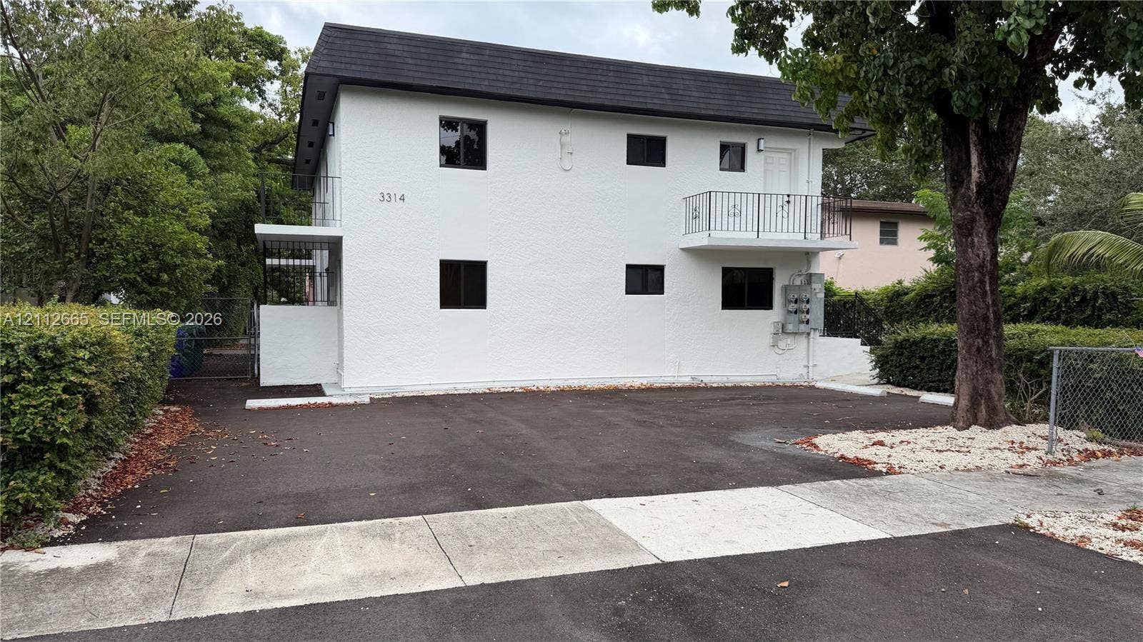 3314 NW 8th, #2, Miami, Miami, FL 33131 Two-story exterior featuring white stucco finish, asphalt roof, private upper-level balcony with metal railing, and dedicated asphalt parking area west side
