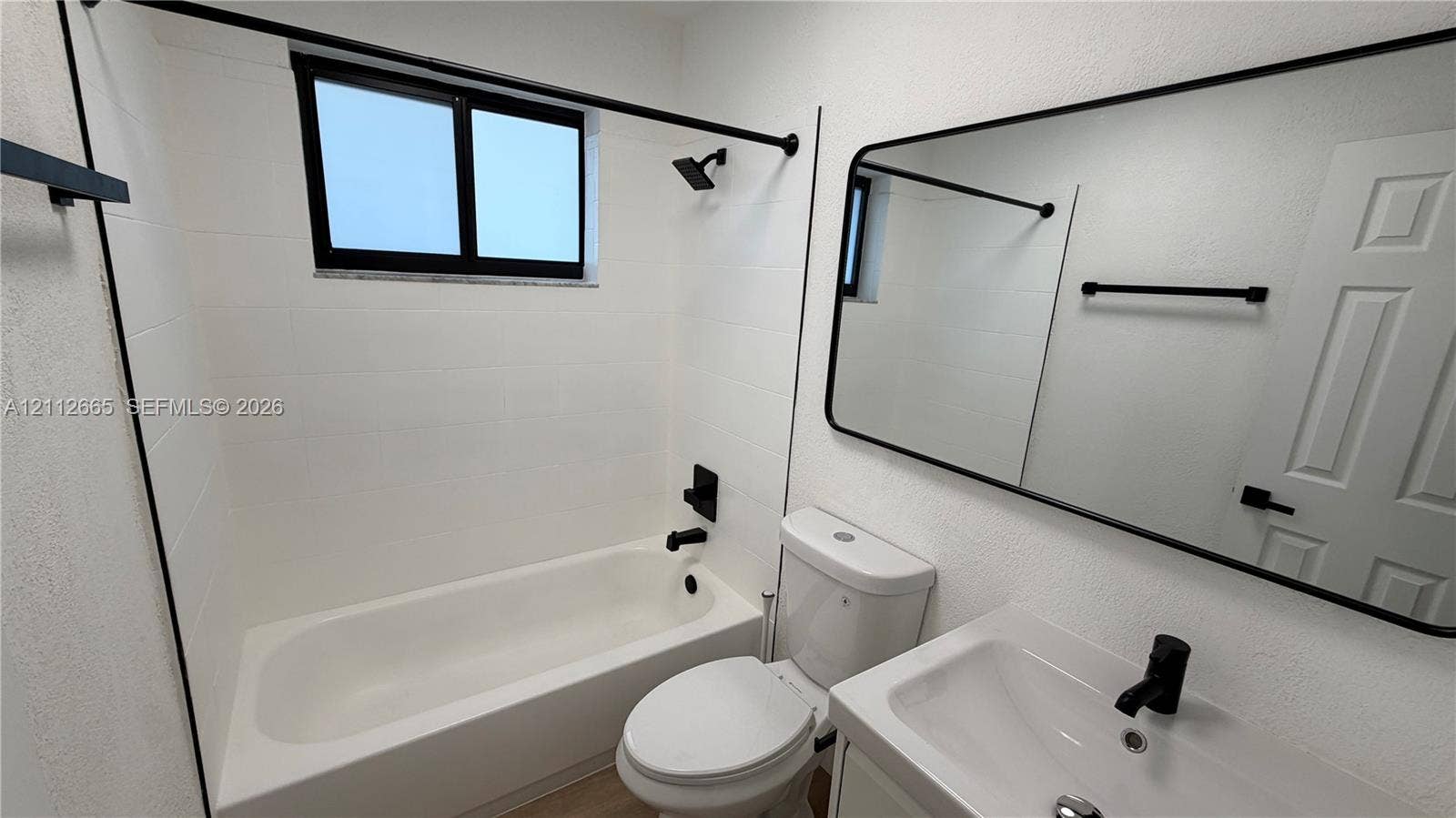 3314 NW 8th, #2, Miami, Miami, FL 33131 Bathroom featuring a white tub-shower combination, modern matte black fixtures, a wall-mounted mirror with a black frame, and a white vanity